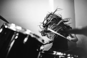 A 9 year old girl has fun playing a drum set in her room, working on songs for her band. High contrast black and white image.